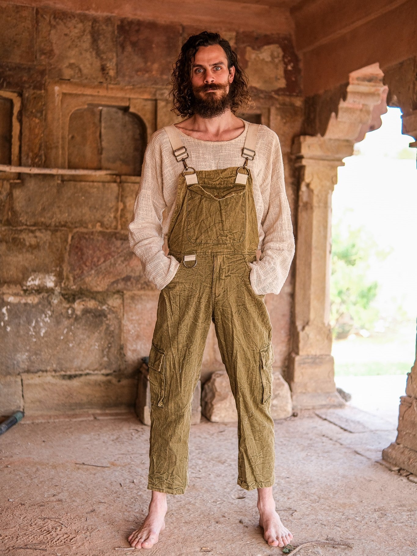 Man wearing green overalls standing in a rustic outdoor setting